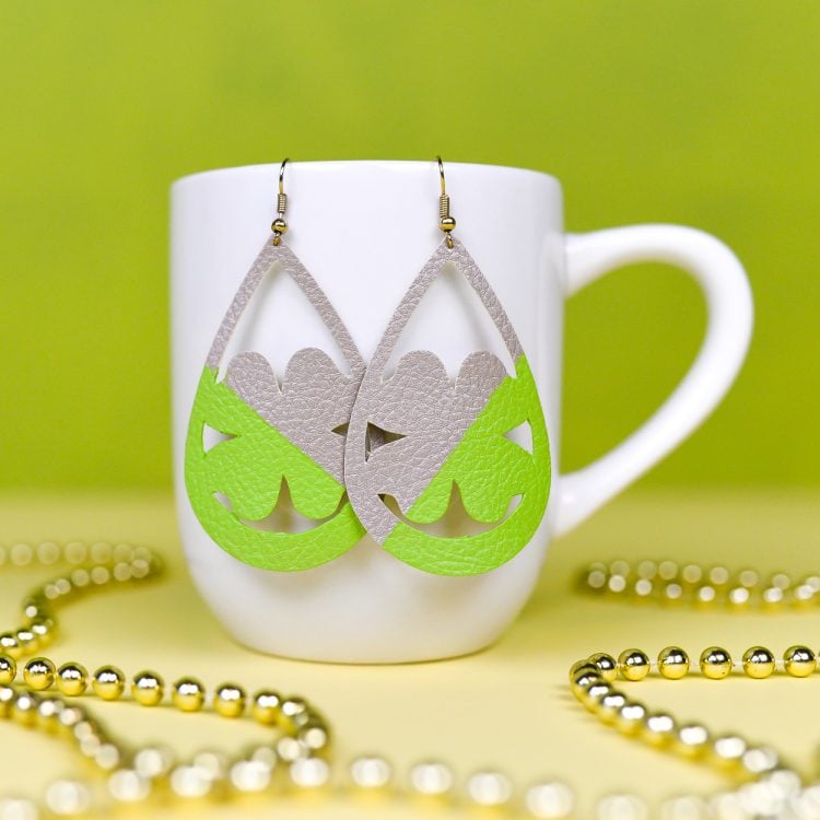 A coffee cup on a table, with Shamrock shaped earrings hanging from it and gold beads next to it