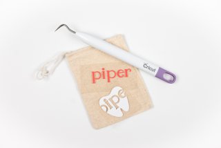 Close up of a small tan pouch, the Cricut weeding tool and the word piper and the image of a tooth on transfer tape