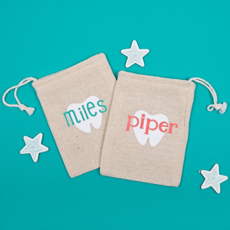 A close up of paper stars around two small tan linen pouches that are decorated with a tooth and personalized with a name