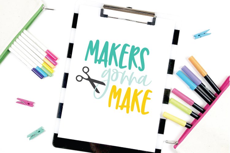 Close up of colorful markers next to a clip board with a piece of paper on it that says, \"Makers Gonna Maker\"