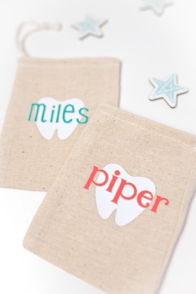 Paper stars around two small tan linen pouches that are decorated with a tooth and personalized with a name