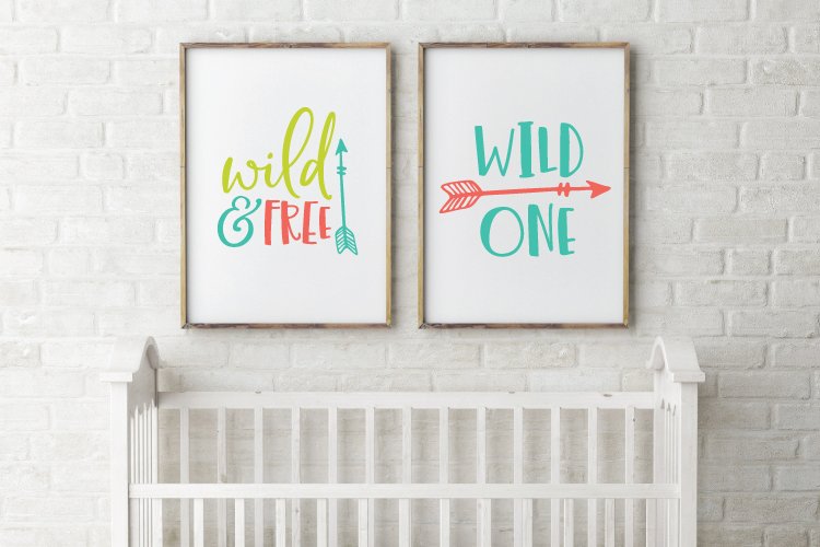 Two framed signs hanging on a brick wall above a baby crib that say, \"Wild & Free\" and \"Wild One\"