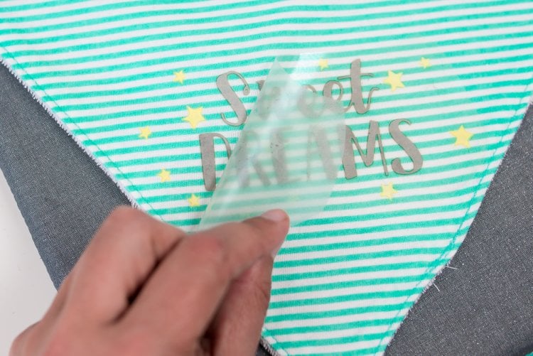 A hand peeling backing from an iron-on design that says, \"Sweet Dreams\"