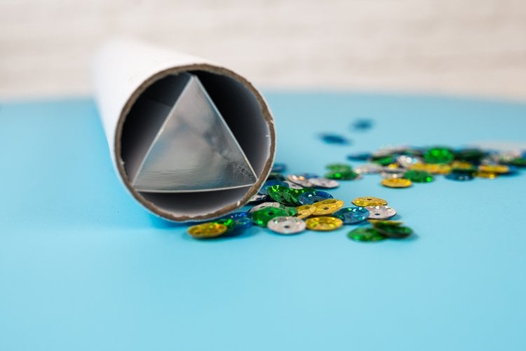 A triangular shaped tube inside of a round tube sitting on a table next to some translucent beads