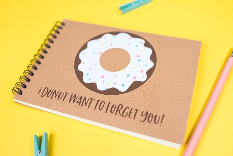 A close up of a pencil, two small clothespins and a journal with an image of a donut on it and text that says, \"I Donut Want to Forget You!\"