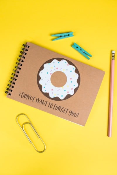 A pencil, a paper clip, two small clothespins and a journal with an image of a donut on it and text that says, "I Donut Want to Forget You!"