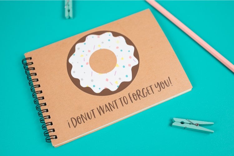A close up of a pencil, two small clothespins and a journal with an image of a donut on it and text that says, \"I Donut Want to Forget You!\"