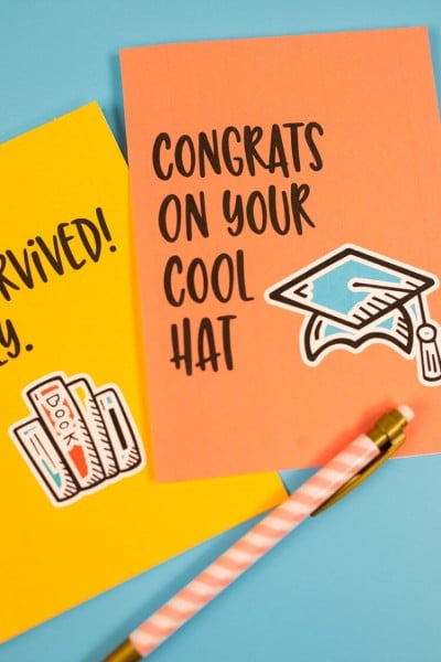 A pen and two greeting cards, one that says, "Congrats on Your Cool Hat"