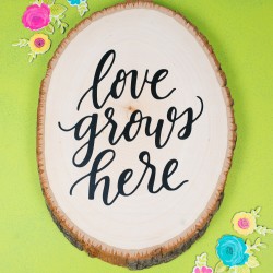 Paper flowers around an oval piece wood with the saying, "Love Grows Here" on it