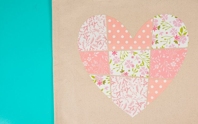 Close up of a tan colored canvas bag with an image of a patchwork heart on it