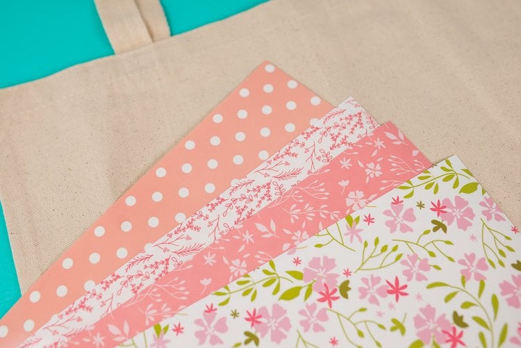 A tan colored canvas bag with four pieces of iron on vinyl on top of it