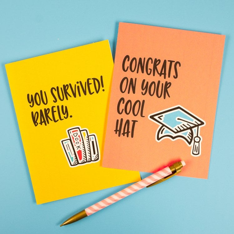 A pen and two graduation cards that say, \"You Survived! Barely\" and \"Congrats on Your Cool Hat\"