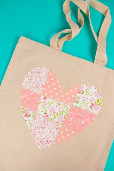 A tan colored canvas bag with an image of a patchwork heart on it