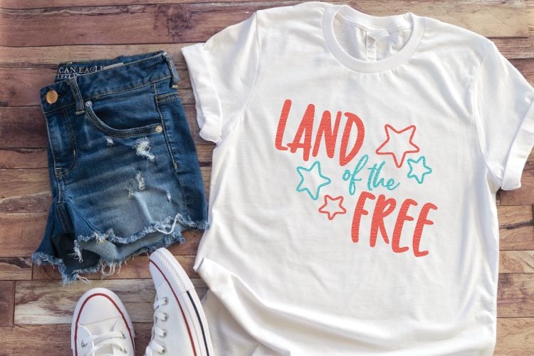 A pair of blue jean shorts, tennis shoes and a white t-shirt decorated with an image of stars and the saying, \'Land of the Free\"