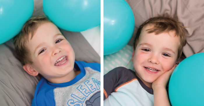 Two little boys lying on a bed with blue balloons around them