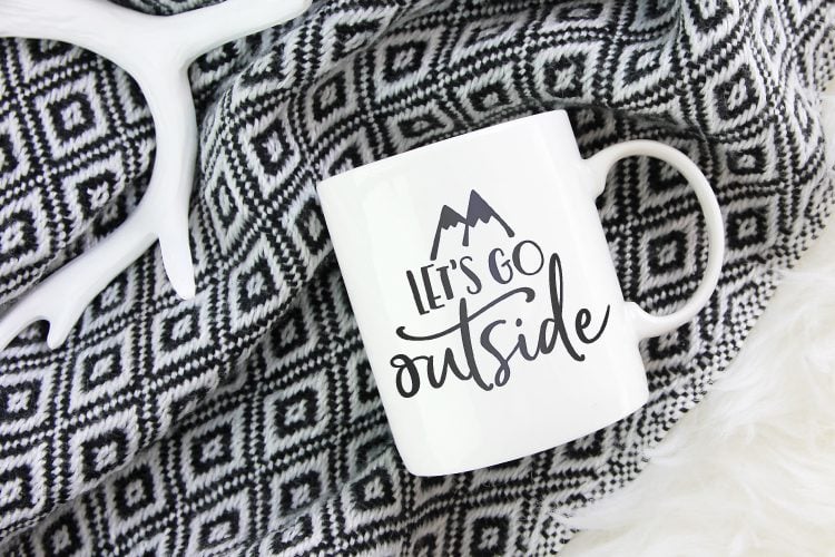 A black and white blanket with a  white coffee cup lying on it, with the saying \"Let\'s Go Outside\"