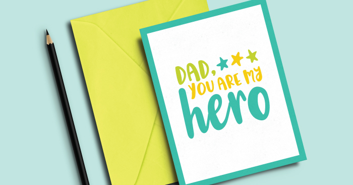 A pencil, and envelope and a greeting card that says, \"Dad, You Are My Hero\"