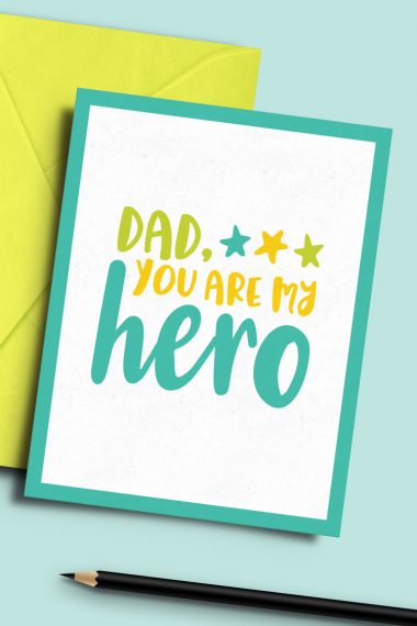 A pencil, and envelope and a greeting card that says, "Dad, You Are My Hero"