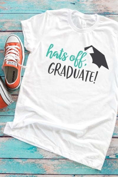 A pair of tennis shoes and a white t-shirt that has an image of a graduation cap and says, "Hats Off, Graduate!"