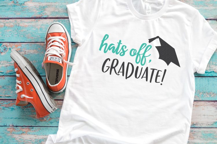 A pair of tennis shoes and a white t-shirt that has an image of a graduation cap and says, \"Hats Off, Graduate!\"