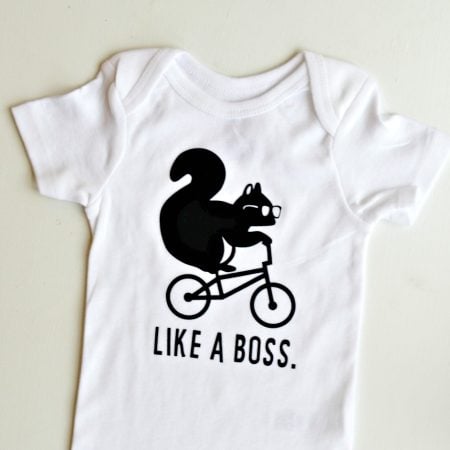A white onesie decorated with a squirrel with glasses on and riding a bike and the saying, "Like A Boss."
