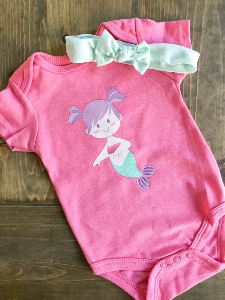 A little baby headband and a pink onesie decorated with an image of a mermaid