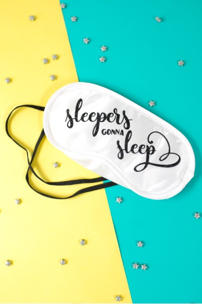Tiny silver stars lying against a yellow and blue background with a white mask that says, "Sleepers Gonna Sleep"