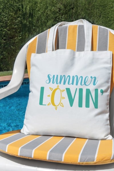 A chair by a pool holding a white canvas bag that says, "Summer Lovin""