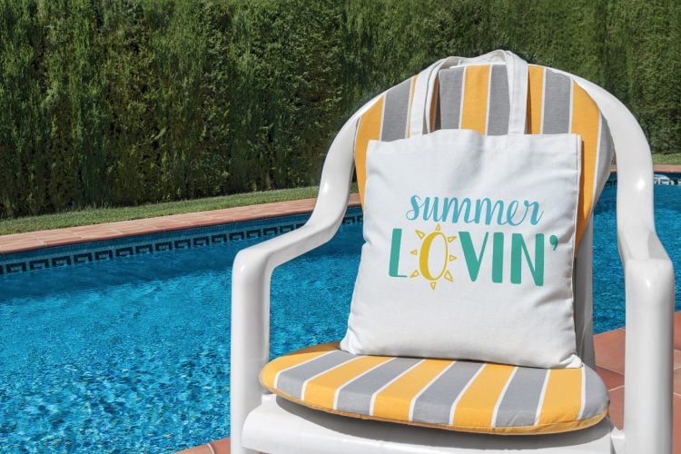 A chair by a pool holding a white canvas bag that says, \"Summer Lovin\"\"