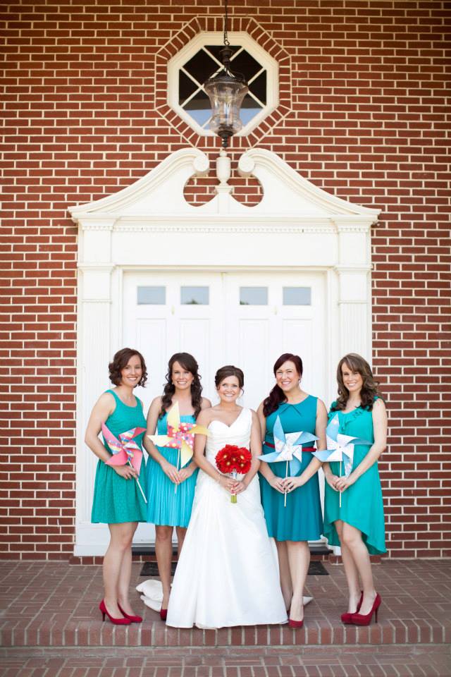 A bride and bridesmaids standing in front of a building and holding flower paper pinwheels