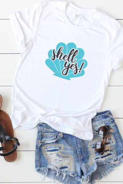 Blue jean shorts, sandals and a white t-shirt decorated with a blue seashell and the saying, "Shell Yes!"