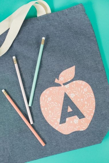 Three pencils on top of a gray canvas bag that is decorated with an image of an apple and the letter 'A' on it