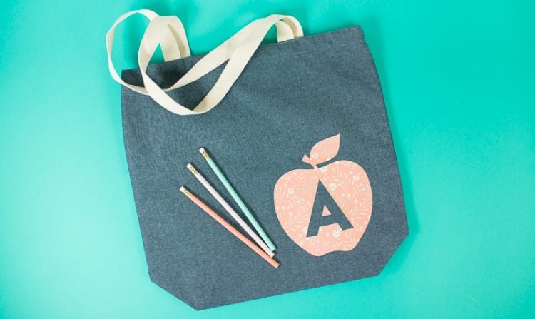 Three pencils on top of a gray canvas bag that is decorated with an image of an apple and the letter \'A\' on it
