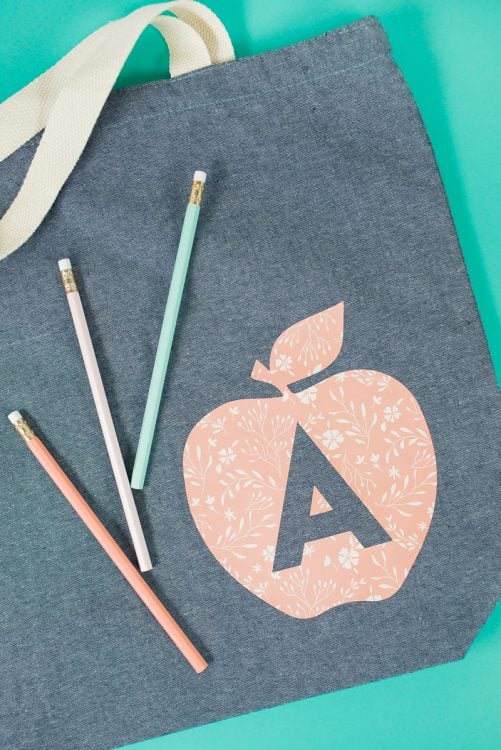 Three pencils on top of a gray canvas bag that is decorated with an image of an apple and the letter 'A' on it