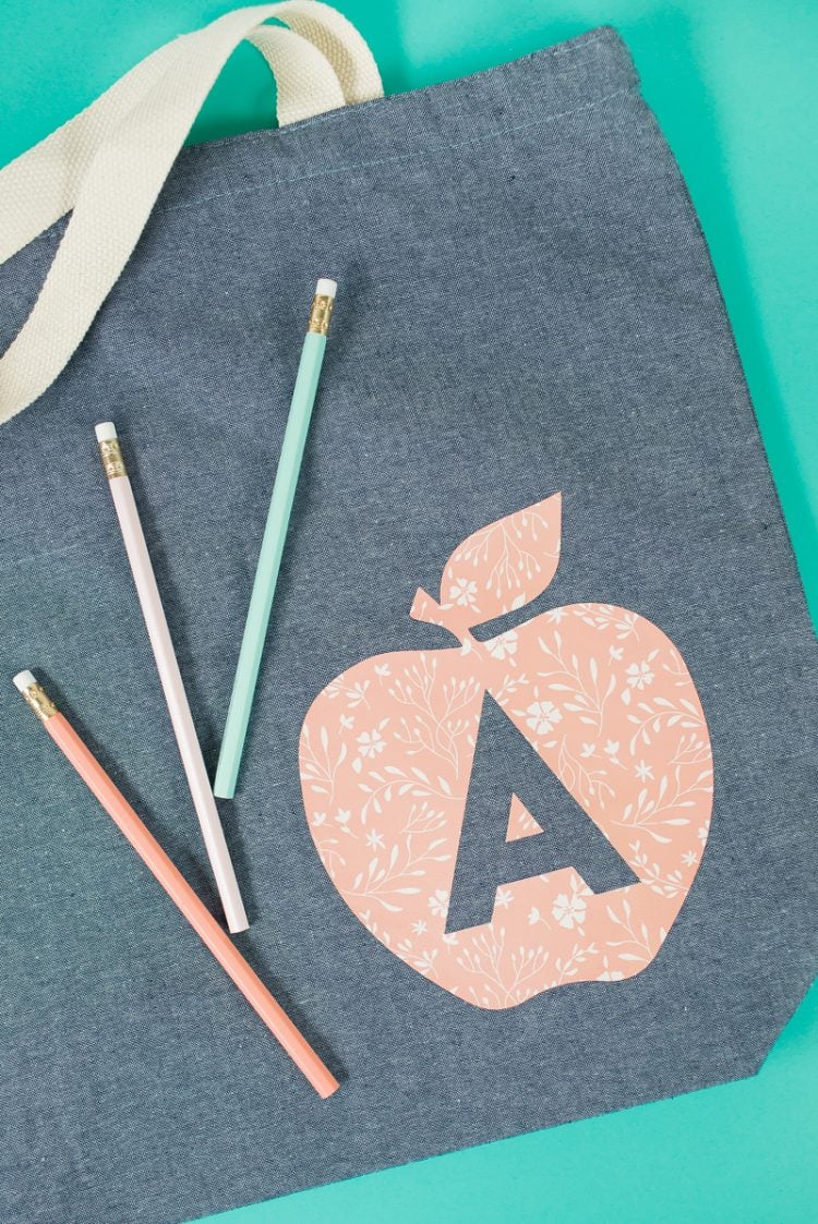 Three pencils on top of a gray canvas bag that is decorated with an image of an apple and the letter \'A\' on it