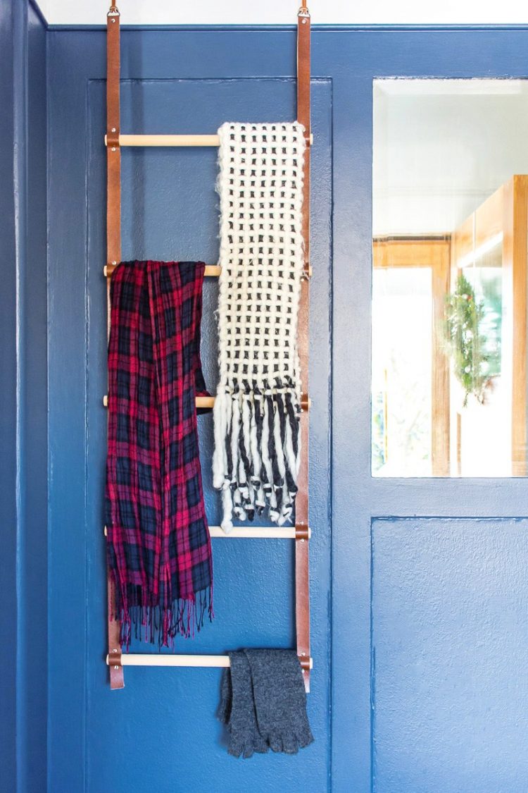 Picture of a ladder hanging against a dark blue wall with scarves hanging from it