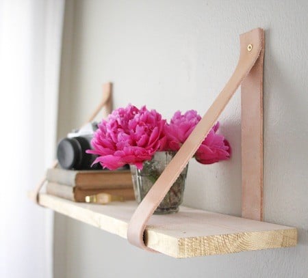 A camera on top of two horizontal books and a vase filled with pink flowers sitting on a wood shelf