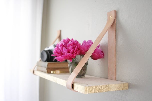 A camera on top of two horizontal books and a vase filled with pink flowers sitting on a wood shelf