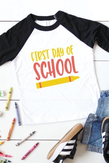 Crayons, sneakers, blue jeans and a black and white baseball style shirt showing a crayon and the text, "First Day of School"
