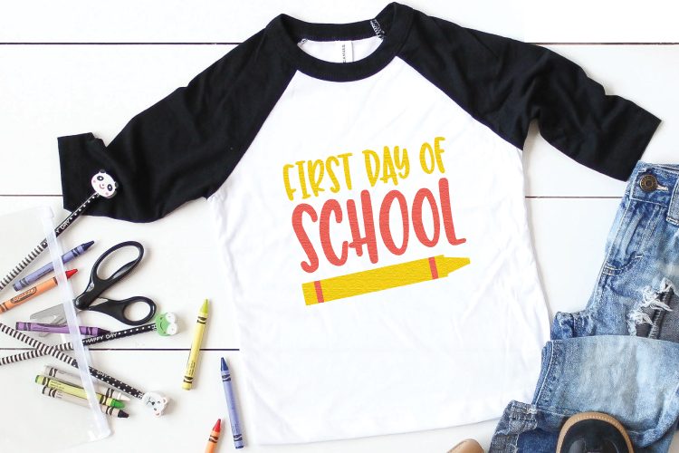 Crayons, pencils, scissors, sneakers, blue jeans and a black and white baseball style shirt showing a crayon and the text, \"First Day of School\"