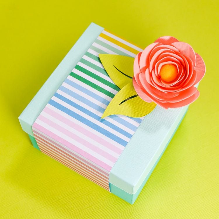 Close up of a box wrapped in multicolored striped paper and a paper rose on top of it