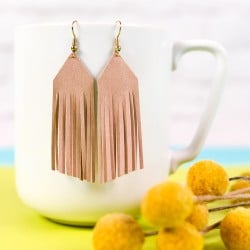 A pair of leather fringed earrings hanging from a coffee cup next to a bouquet of flowers