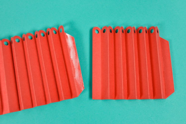 Accordion folded red paper that has holes punched in the top of each fold