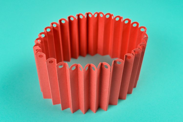 Accordion folded red paper that has holes punched in the top of each fold