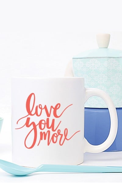 A canister sitting next to a spoon and a coffee mug.  The mug is decorated with the text, "Love You More"