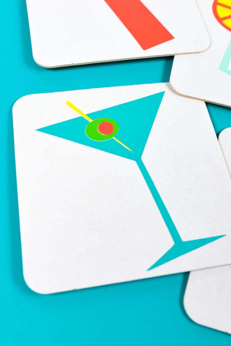 Close up of a white coaster decorated with an image of a martini glass with an olive in it