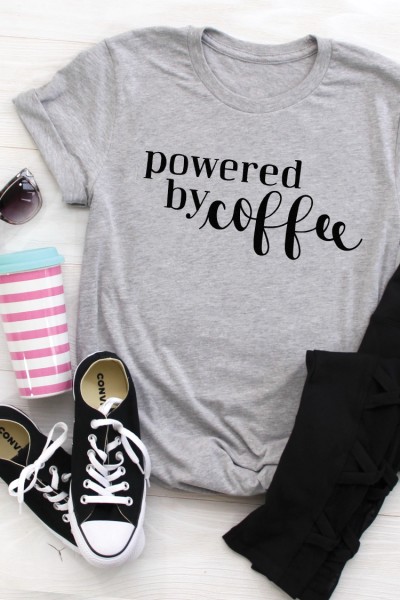 A pair of sunglasses, tennis shoes, black jeans, coffee tumbler and a gray t-shirt that says, "Powered by Coffee"