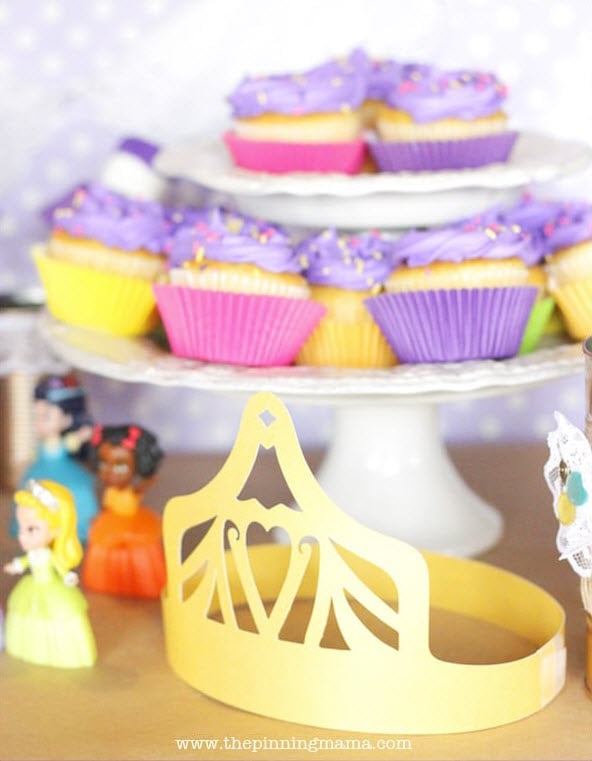 A tray of cupcakes, a paper crown and figurines of Disney princesses