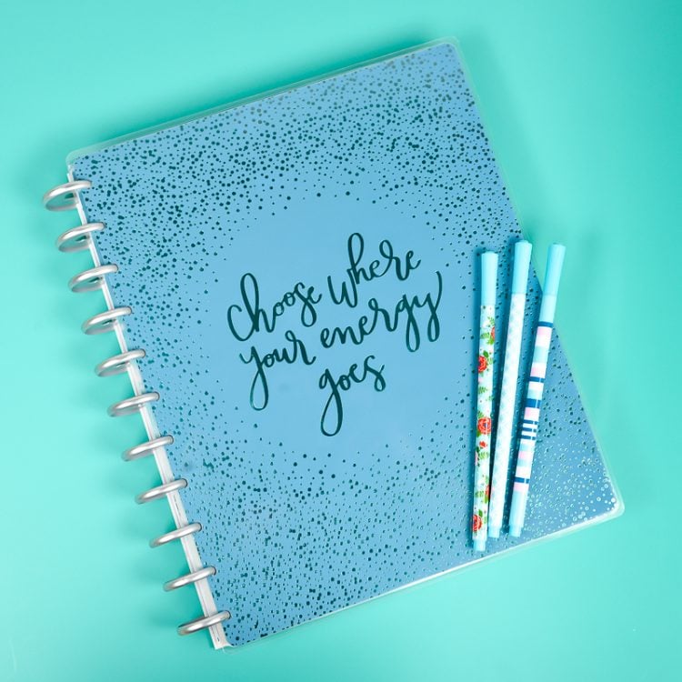 Pens on top of a journal that is decorated with the text, \"Choose Where Your Energy Goes\"