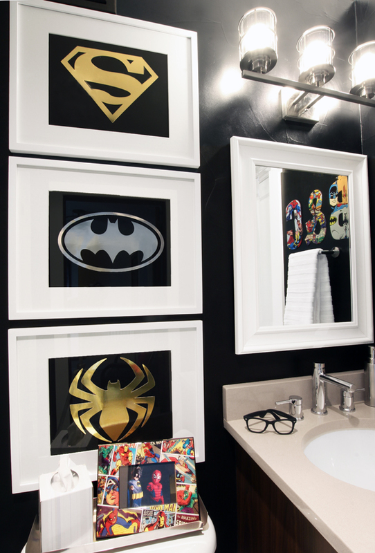 A bathroom with a sink and a mirror with Superhero art hanging on the wall and a framed superhero picture on the back of the toilet